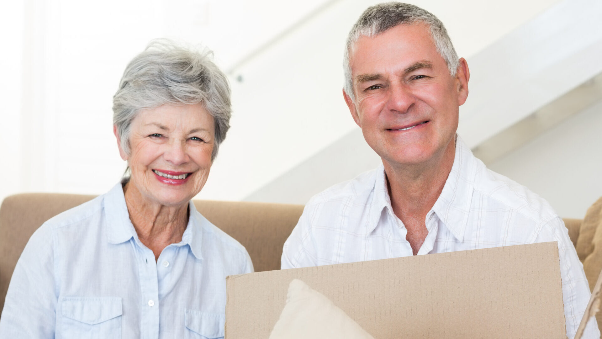 Elderly couple sitting on couch packing box for move.